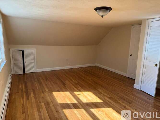 A room with wooden flooring and white walls, with a window on the left and a door on the right.