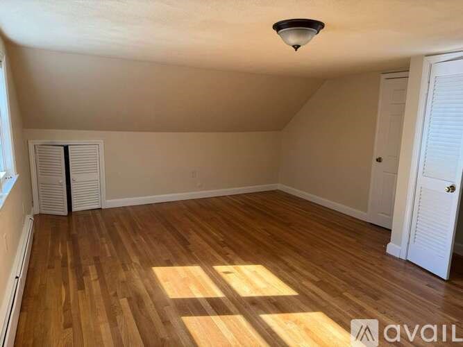 A room with wooden flooring and white walls, with a window on the left and a door on the right.