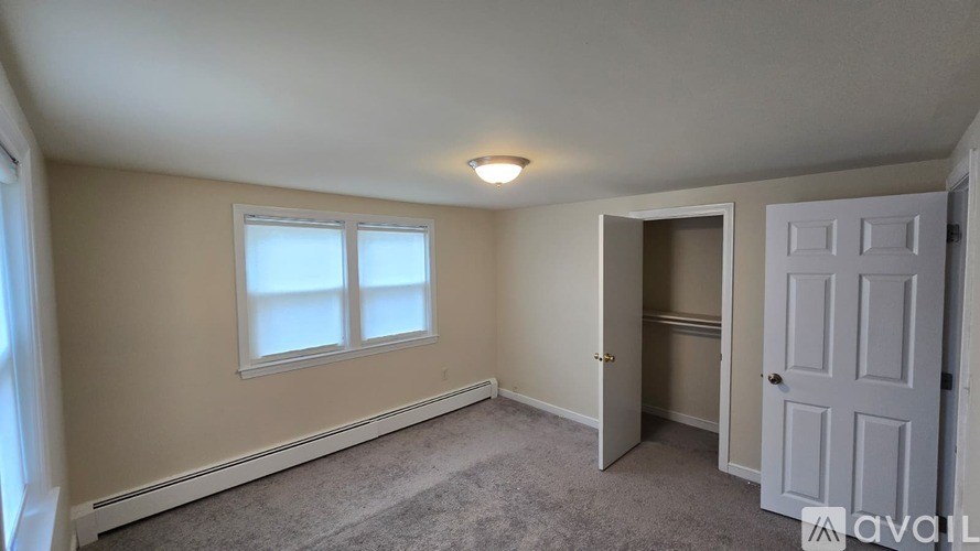 A room with a carpeted floor, a window with white blinds, a white door, and a ceiling light fixture.