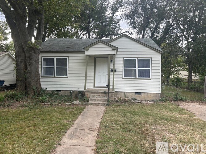 A small house with a white door and windows is surrounded by trees.