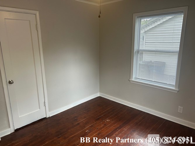 A room with a door, a window, and a wooden floor.