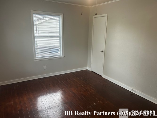 A room with a wooden floor and a window with blinds.