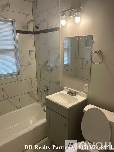 A bathroom with a marble tile shower, a white toilet, and a sink.