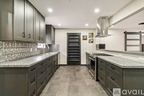 A modern kitchen with dark cabinets and a marble countertop.