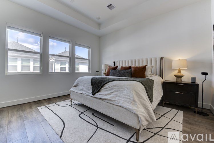 A bedroom with a large bed, a nightstand with a lamp, and a window with a view of a house.