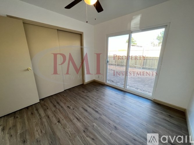 A room with wooden flooring and a ceiling fan, with a window showing an outdoor fence.