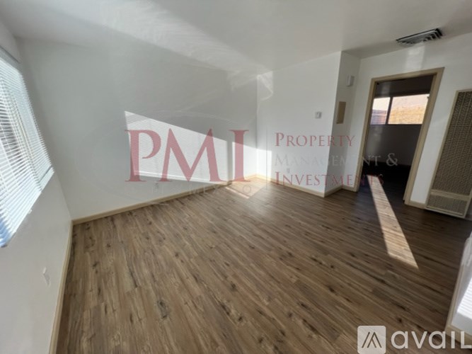 A room with wooden flooring and white walls, with a window on the left side.