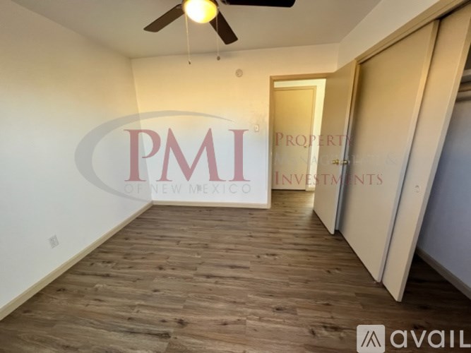A room with wooden flooring and a ceiling fan, with a logo for PMI Property Investments of New Mexico on the wall.