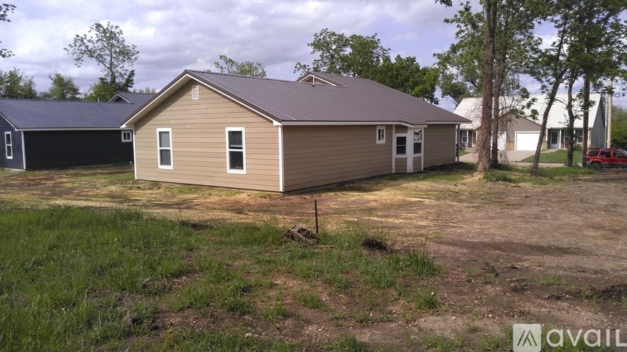 A house with a brown roof and beige siding is surrounded by a grassy area and trees.