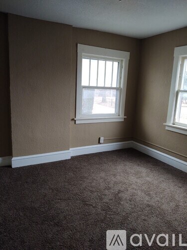 A room with brown carpet and two windows.