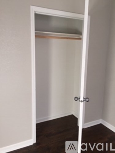 A white door with a silver handle is open to a room with a white wall and a wooden floor.