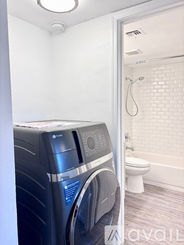 A washing machine is in a bathroom with a toilet and a shower.