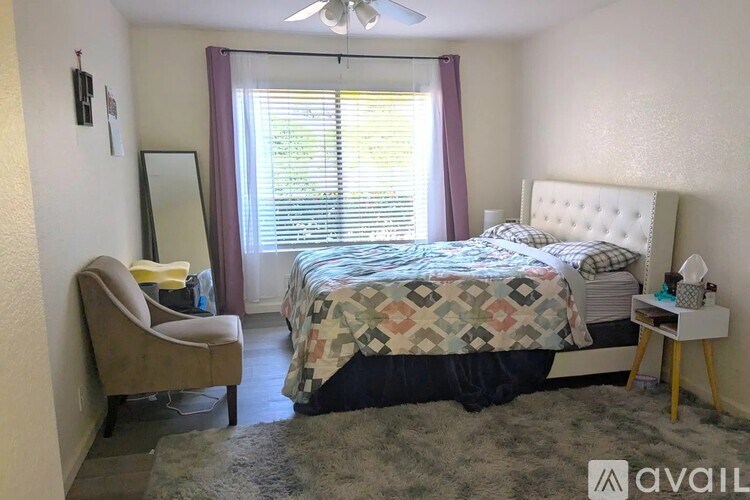 A bedroom with a bed, chair, and a fan.