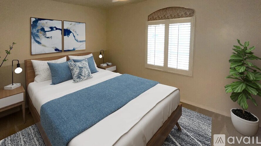 A bedroom with a bed, two lamps, a plant, and a painting on the wall.