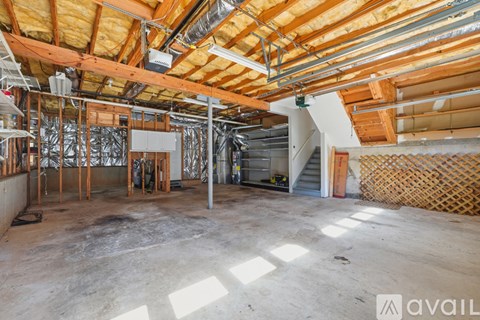 A large, empty room with wooden beams on the ceiling and a staircase on the right side.