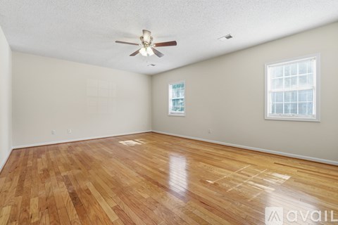 A room with a chandelier, a window with blinds, and wooden flooring.