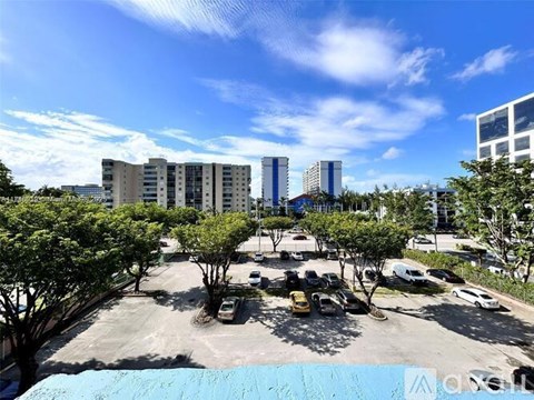A parking lot with cars and trees in front of apartment buildings.