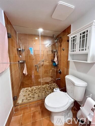 A small bathroom with a toilet, a shower with a glass door, and a white cabinet above the toilet.
