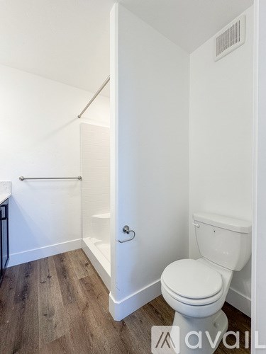 A white toilet in a small bathroom with wood flooring and a white shower stall.