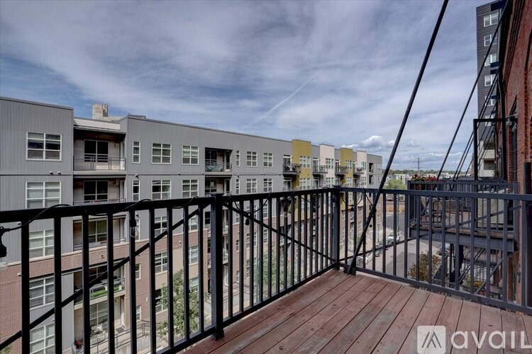 A balcony with a black railing and a wooden floor overlooks a row of buildings.