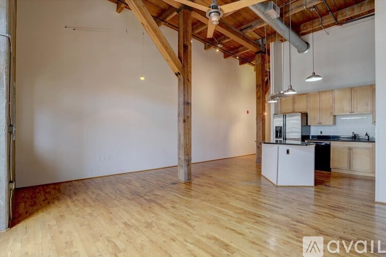 A room with wooden floors and a kitchen area with white appliances.