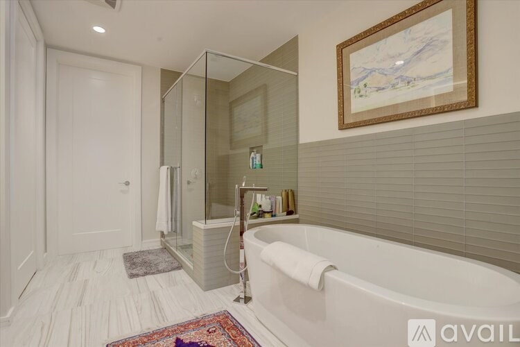 A bathroom with a white tub, a rug, and a painting on the wall.