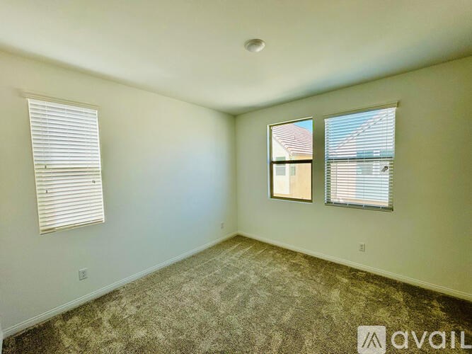 A room with a carpeted floor, two windows with blinds, and a ceiling light fixture.