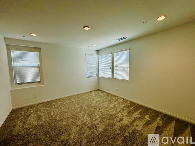 A room with carpeted floor, two windows with blinds, and a ceiling with recessed lighting.