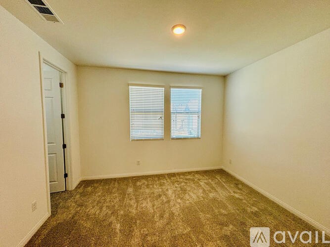 A room with a carpeted floor, a window with blinds, and a door.