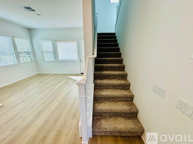 A staircase with a carpeted runner leads up to a bright room with wooden floors and windows.