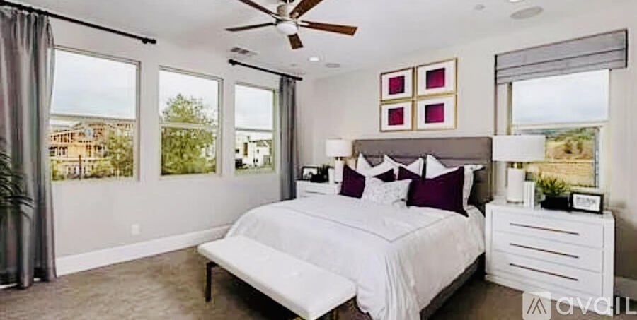 A bedroom with a large bed, a ceiling fan, and a view of the outdoors through the windows.