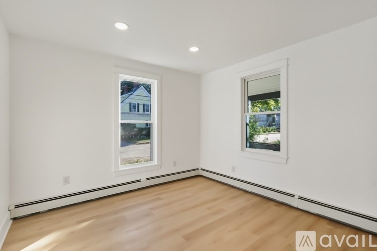 A room with wooden floors and two windows, one of which has a view of a blue house.