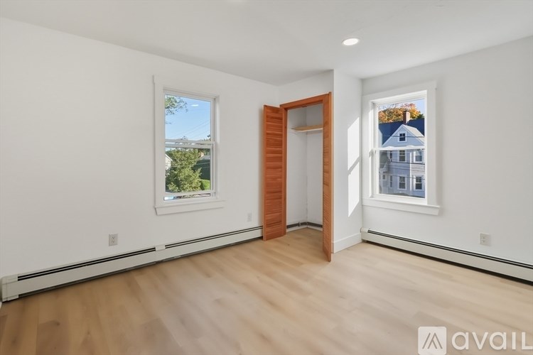 A room with a wooden floor and white walls, with a window showing a blue house outside.
