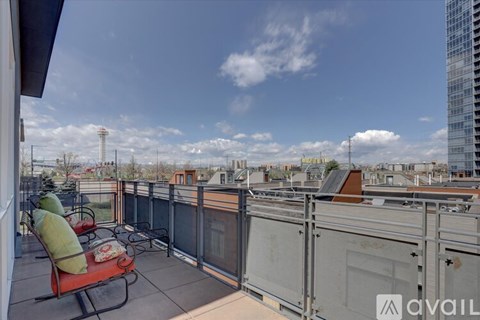 A balcony with a red chair and a table is overlooking a cityscape.
