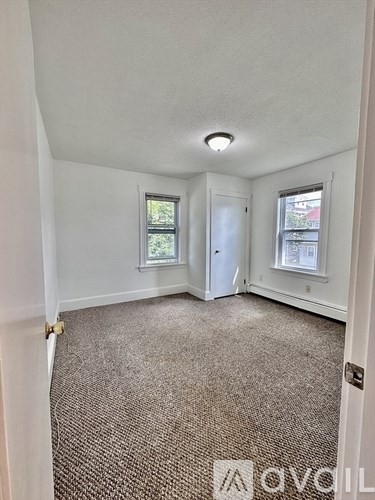 A carpeted room with a door and a window.
