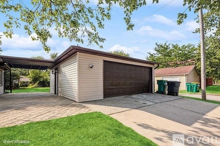 A detached garage with a brown roof and a grey garage door is surrounded by a green lawn and trees.