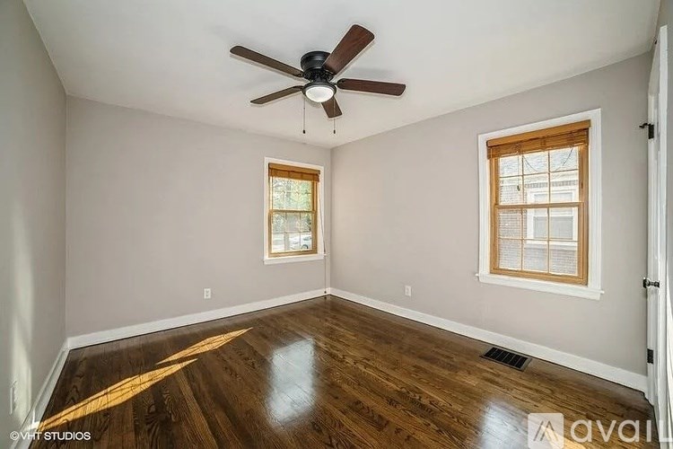 A room with a ceiling fan and two windows.