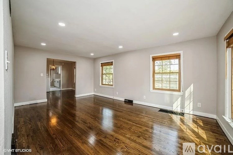 A spacious room with wooden floors and two windows.