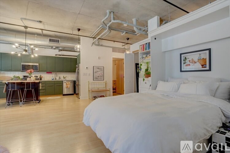 A bedroom with a large bed and a kitchen area in the background.
