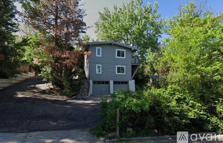 A house with a grey and white exterior is surrounded by greenery.