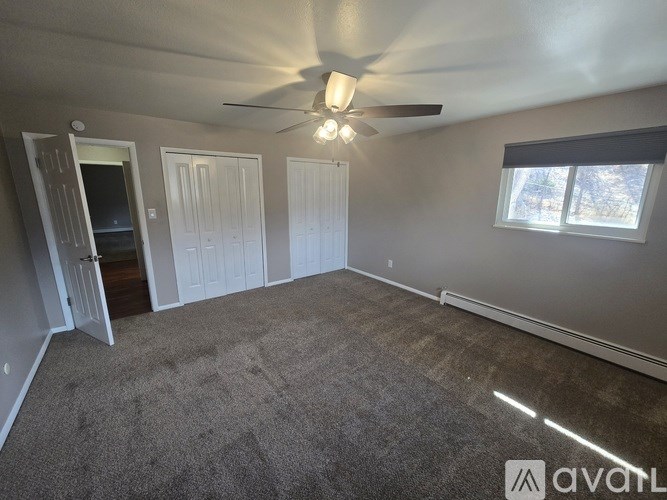 A room with a carpeted floor, a ceiling fan, and a window with blinds.