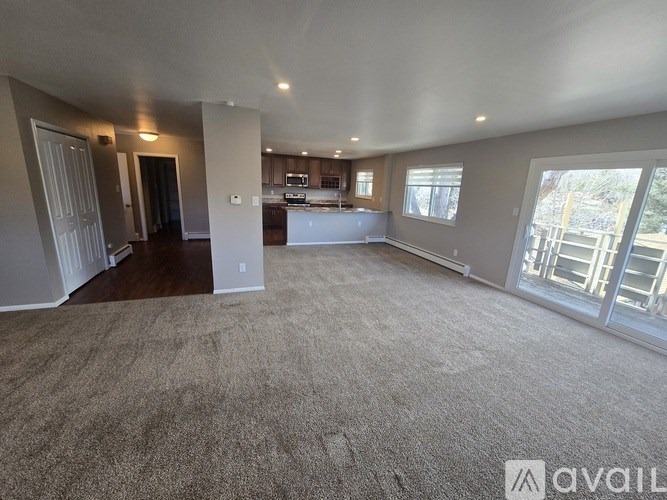 A spacious living room with a carpeted floor and a kitchen area in the background.