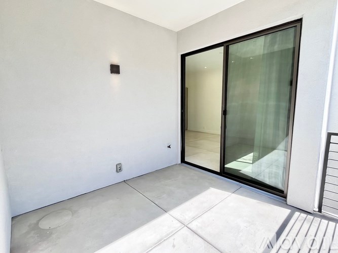 A white room with a glass door and a small black square on the wall.