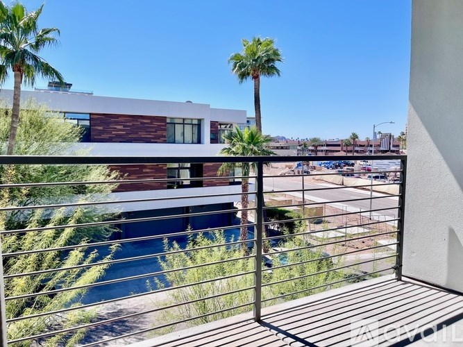 A balcony with a metal railing overlooks a pool and palm trees.
