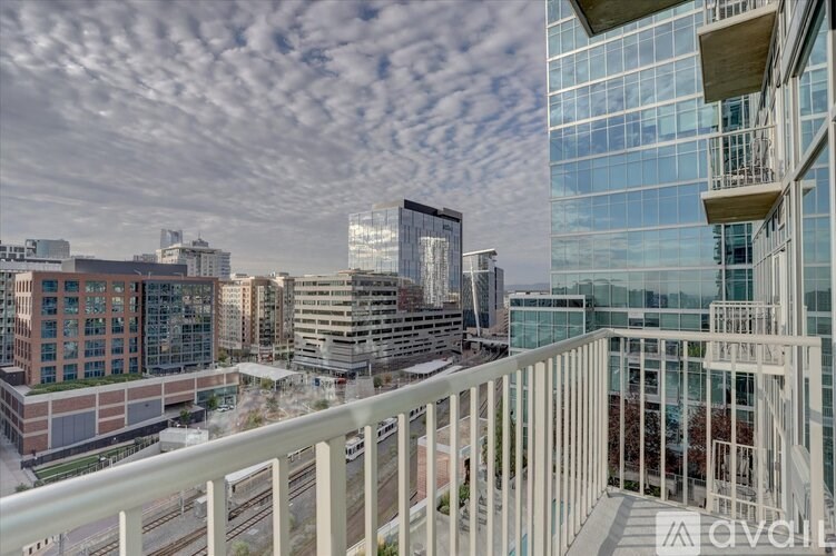 A modern cityscape with a clear sky and a balcony in the foreground.