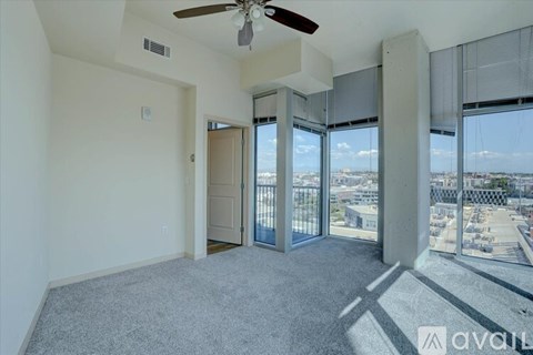 A room with a ceiling fan and large windows overlooking a cityscape.