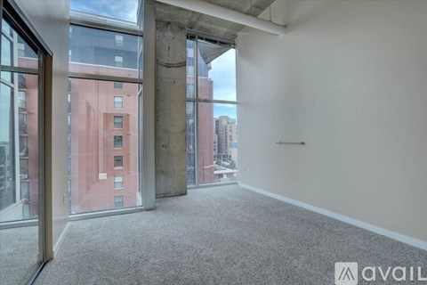 A room with a carpeted floor and large windows overlooking a cityscape.