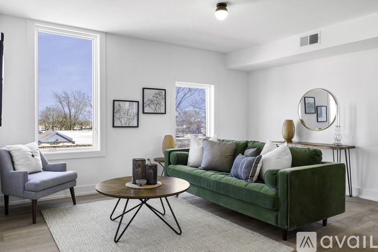 A living room with a green couch, grey armchair, and a round table with a vase on it.