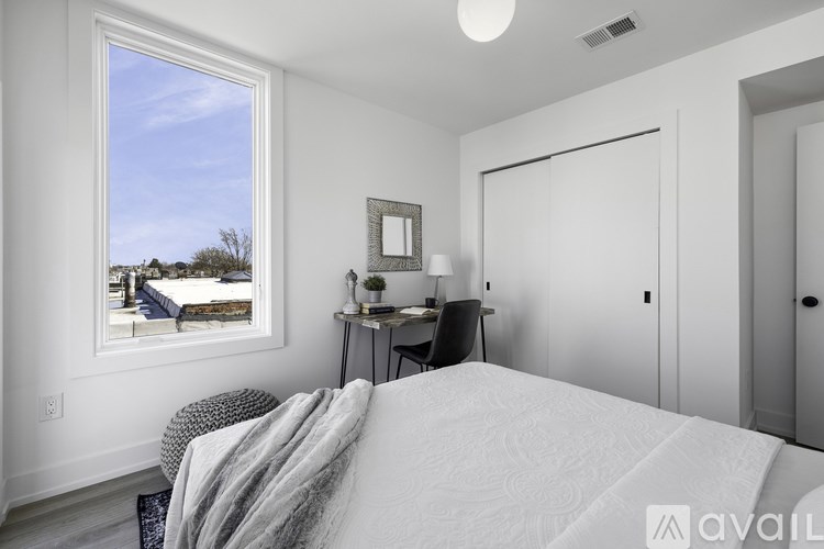 A bedroom with a large bed, a desk with a chair, and a window overlooking a residential area.