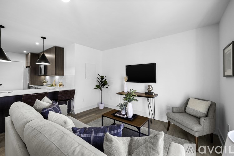 A living room with a grey couch, a coffee table, a chair, and a flat screen TV mounted on the wall.